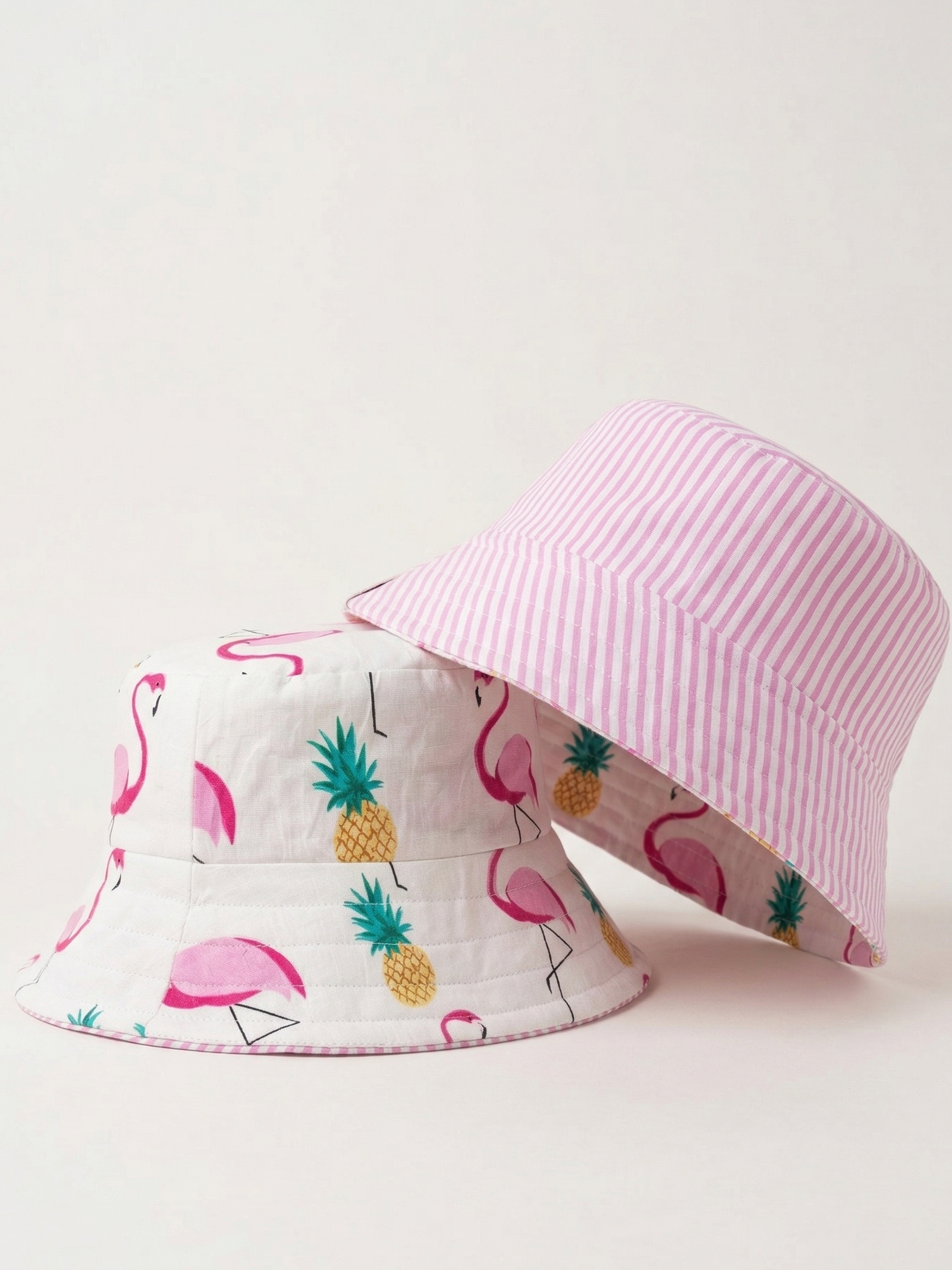 Two bucket hats with flamingo and pineapple pattern on a light pink background
